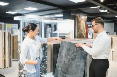 Seramik ve sıhhi tesisat dükkanında çalışan bir kadına farklı seramik fayans örnekleri gösteren bir tezgahtar.