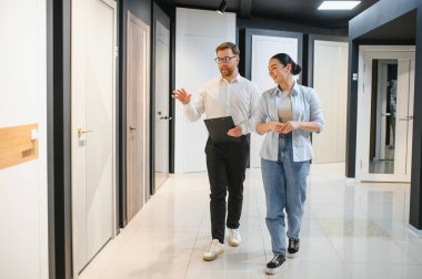 Bir kadın müşteriye hırdavatçıda rehberlik ediyor, çeşitli iç kapı seçeneklerini tartışıyor ve stil ve tasarımları keşfediyor.