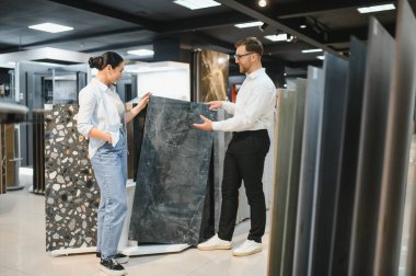 Mağazadaki kadın müşteriye seramik fayans seçenekleri gösteren bir mağaza asistanı