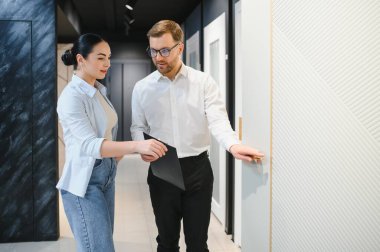 Satıcı, bir tesisat ve fayans dükkanında klasör tutan kadına iç tasarım seçenekleri gösteriyor.