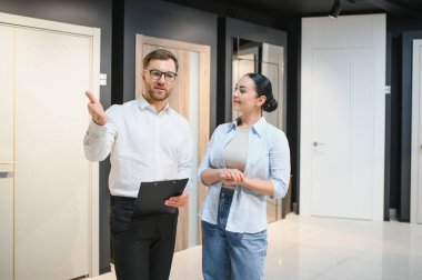 Profesyonel mağaza asistanı elinde pano tutarak kapı ve pencerelerde kadınlara iç tasarım çözümleri gösteriyor