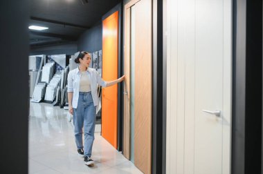 Çağdaş bir seramik fayans ve tesisat dükkanının kapılarını inceleyen kadın müşteri, iç tasarım seçeneklerini ve ev yenileme malzemelerini ön plana çıkarıyor.