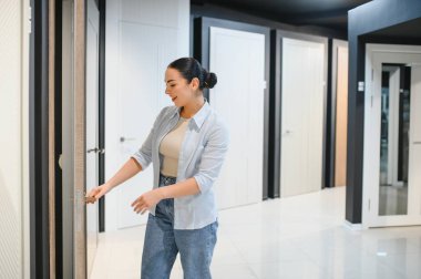 Ev dekorasyonu mağazasında kapıları seçen, kapı koluna dokunan, kalite ve tasarımı kontrol eden, satın alma kararı veren bir kadın.