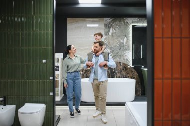Mutlu bir aile seramik fayans ve su tesisatı dükkanında banyo demirbaşlarını seçiyor. Oğullarını omuzlarında taşıyorlar.