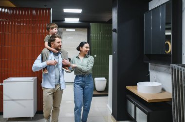 Genç bir aile seramik fayans ve tesisat dükkanını ziyaret ederek, ev yenileme projeleri için modern tesisat ve tasarım seçeneklerini inceliyor.