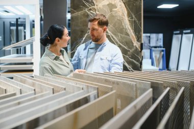 Hırdavatçıda yenilemek için seramik fayanslar seçen çift, çeşitli örnekleri tartışıyor ve seçiyor.