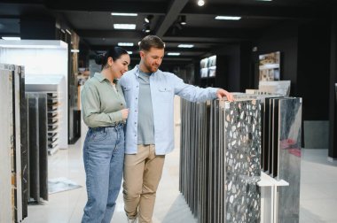 Çift, bir tesisat ve fayans dükkanında çeşitli seramik fayanslar inceleyerek, ev yenileme veya dekorasyon seçeneklerini değerlendiriyor