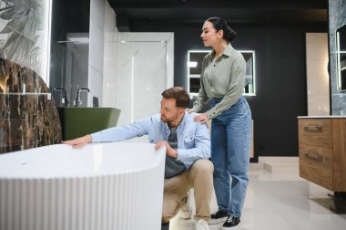 Çağdaş bir seramik fayans ve su tesisatı dükkanında küveti inceleyen çift, ev yenileme ve iç tasarım çalışmalarına ilgi gösteriyor.
