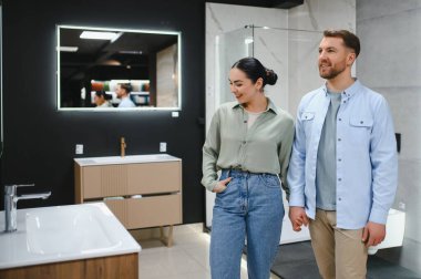 Ev dekorasyonu mağazasının vitrininde yürürken modern banyo eşyalarına bakan çift el ele tutuşuyor.