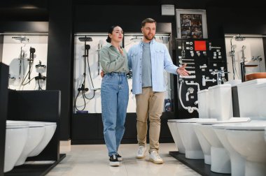 Genç çift yeni tuvalet kapağını bir su tesisatçısı olarak seçiyor, farklı modelleri tartışıyor ve işaret ediyorlar.