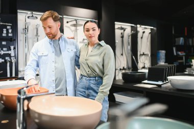 Modern bir tesisat ve seramik dükkanında modern ev geliştirme seçenekleri sunan şık lavaboları ve demirbaşları inceleyen çift.