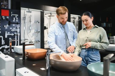 Genç çift bir su tesisatçısında seramik lavabo seçiyorlar, yüzeye dokunuyorlar ve alışverişlerini tartışıyorlar.