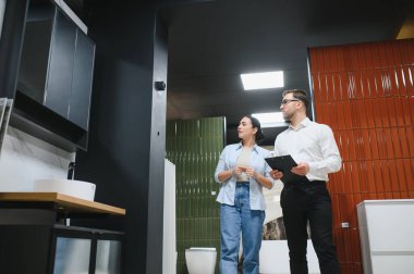 Satış asistanı, seramik ve tesisat perakende mağazasında çeşitli banyo armatürlerini sergiliyor.