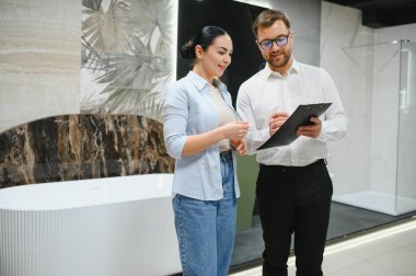 Satış elemanı, müşteriye seramik fayanslar ve sergi odasındaki banyo demirbaşlarını seçmesinde yardımcı olurken not alıyor.
