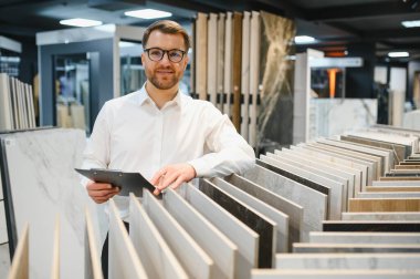 Modern bir tesisat ve fayans dükkanında müşteriye farklı seramik fayans örnekleri gösteren bir satıcı.