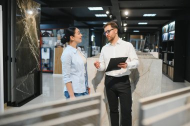 Profesyonel satıcı, bir kadın müşteriye farklı seramik örnekler gösteriyor. Modern bir galeride yenileme projesi için malzeme tartışıyor ve seçiyor.