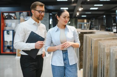 Modern bir hırdavatçıda kadın müşteriye farklı seramik örnekler gösteren bir tezgahtar.
