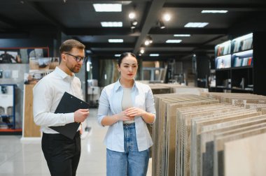 Satıcının elinde elinde seramik fayans örnekleri var. Tesisat ve fayans dükkanlarındaki düşünceli kadın müşteriye.