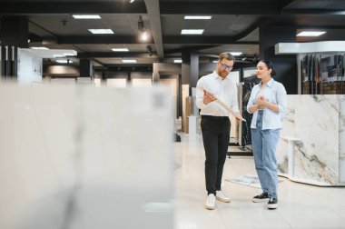 Satış elemanı, bir bayan müşteriye parlak, modern fayanslar ve tesisat mağazasında seramik fayanslar seçmesinde yardımcı oluyor, seçenekleri ve stilleri tartışıyor.