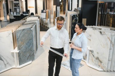 Satıcının seramik fayans seçeneklerini bir seramik ve tesisat mağazasında sunması ev iyileştirme seçenekleri üzerine bir tartışmayı kolaylaştırıyor.