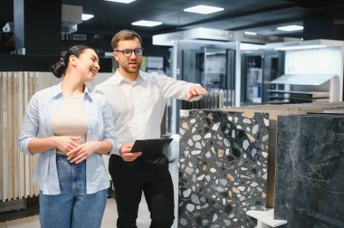 Satıcı, bir inşaat malzemeleri dükkanındaki kadın müşteriye farklı seramik fayanslar gösteriyor.