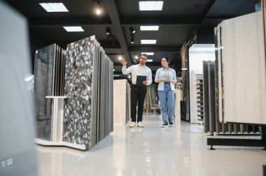 Modern bir hırdavatçıda kadın müşteriye farklı seramik fayanslar gösteren bir satıcı.