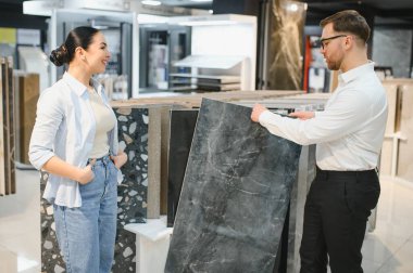 Seramik seramik ve sıhhi tesisat mağazasında müşteriye seramik fayans örnekleri sunan mağaza asistanı seçim sürecini kolaylaştırıyor.