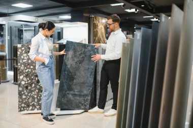 Satış elemanı seramik ve su tesisatı mağazasındaki müşteriye seramik ve su tesisatı seçeneklerini sunuyor, ev geliştirme projelerinin stillerini tartışıyor.