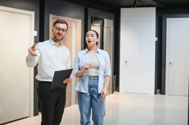 Satış elemanı bir ev geliştirme mağazasında müşteriye çeşitli iç kapı seçenekleri sunuyor, seçenekleri kolaylaştırıyor ve yenileme planlarını geliştiriyor