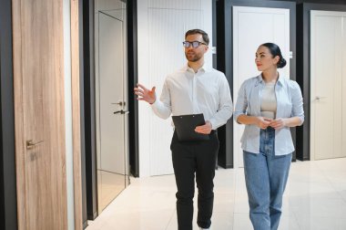 Satıcı, bina malzemeleri mağazasına giren kadın müşteriye iç ve giriş kapılarını gösteriyor.