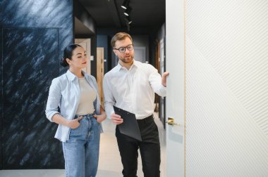 Satış elemanı, seramik fayans ve tesisat mağazasındaki kadın müşterilere iç tasarım seçeneklerini gösteriyor.