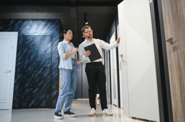 Profesyonel mağaza asistanı seramik fayans ve tesisat mağazasında pano tutan modern beyaz kapıyı bayan müşteriye gösteriyor.