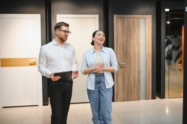 Gülümseyen bayan müşteri satış elemanının ev dekorasyonu mağazasındaki yeni kapıların özelliklerini dinledi.