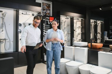 Profesyonel satıcı, kadın müşterilere farklı banyo armatürleri gösteriyor. Su tesisatında pano tutuyor.