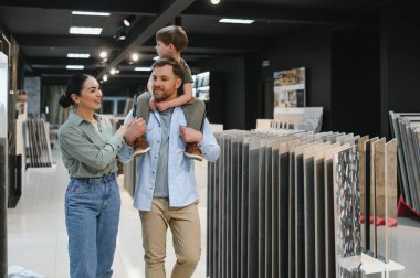 Mutlu bir aile, özel bir mağazada yenilemek için seramik fayanslar seçiyor. Oğulları da babalarının omuzlarında oturuyor.