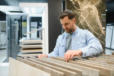 Modern bir sergi odasında seramik fayansları seçen mimar, şık bir mekanda yeni bir iç tasarım projesi için seçenekleri dikkatlice değerlendiriyor