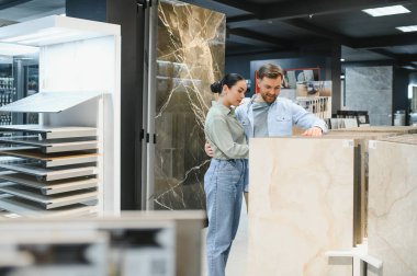 Genç çift, modern bir hırdavatçıda dairelerini yenilemek için seramik fayanslar seçiyor, kucaklıyor ve gülümsüyor.