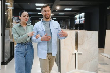 Çift, modern bir tesisat ve fayans dükkanında seramik fayans seçeneklerini tartışırken ve incelerken görülüyor.