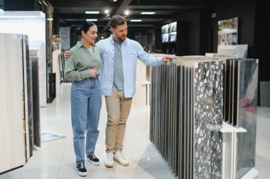 Genç çift, dairelerini yenilemek için seramik fayanslar seçerken modern bir hırdavatçıda çeşitli seçeneklerin tadını çıkarıyor.