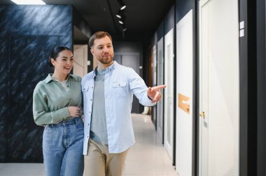 Mutlu çift iç kapıları işaret ediyor, seramik fayans ve tesisat dükkanında ev dekorasyonu için eşyalar seçiyorlar.