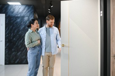 Mutlu çift yeni bir iç kapı seçiyor, bir ev geliştirme mağazasında birbirlerine sarılıyorlar, yenileme projeleri için en uygun yeri arıyorlar.