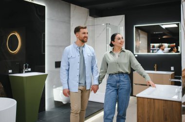 Mutlu çift el ele tutuşup seramik fayanslar ve modern banyo demirbaşlarını seçiyor.