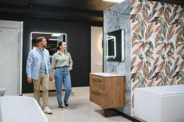 Modern banyo eşyaları ve seramik fayans tasarımlarını inceleyen çift iyi aydınlatılmış bir tesisat ve ev dekorasyonu mağazasında çalışıyor.