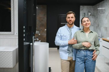 Modern eşyalar ve şık banyo vitrinleriyle çevrili seramik fayans ve su tesisatı dükkanını ziyaret eden gülümseyen bir çift.
