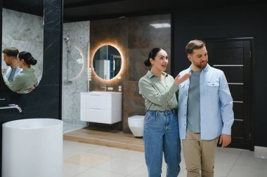 İç mimar seramik fayans ve tesisat dükkanındaki müşteriye banyo armatürlerini gösteriyor.