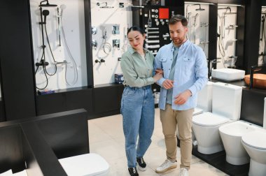 Genç çift, tesisat mağazasında yeni banyo tesisatı seçiyor, seçenekleri tartışıyor ve evlerinin yenilenmesi için karar veriyorlar.