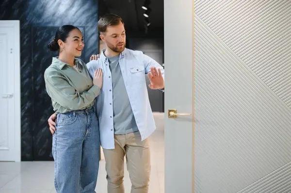 Mutlu çift mobilya ve nalbur dükkanında yeni bir iç kapı seçiyor kucaklaşıp gülümsüyor, kapıya dokunuyor.