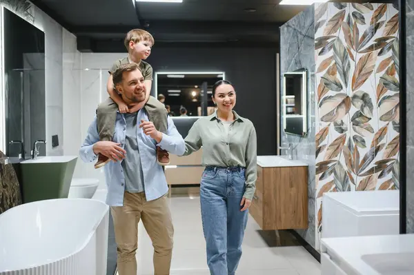 Gülümseyen bir aile bir tesisat dükkanında birlikte yürüyor, seramik fayanslar ve banyo dekorasyonu projeleri için eşyalar seçiyorlar.