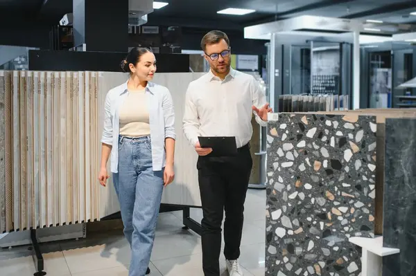 Satış elemanı bir tesisat mağazasında müşteriye çeşitli seramik fayanslar sunuyor, ev geliştirme projeleri için seçenekleri ve stilleri tartışıyor.