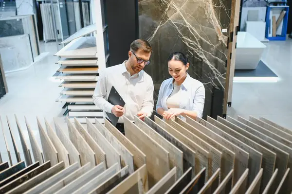 Tuvaleti için seramik fayanslar seçen gülümseyen bir bayan müşteri, elinde bir pano tutan bir mağaza asistanından yardım aldı.